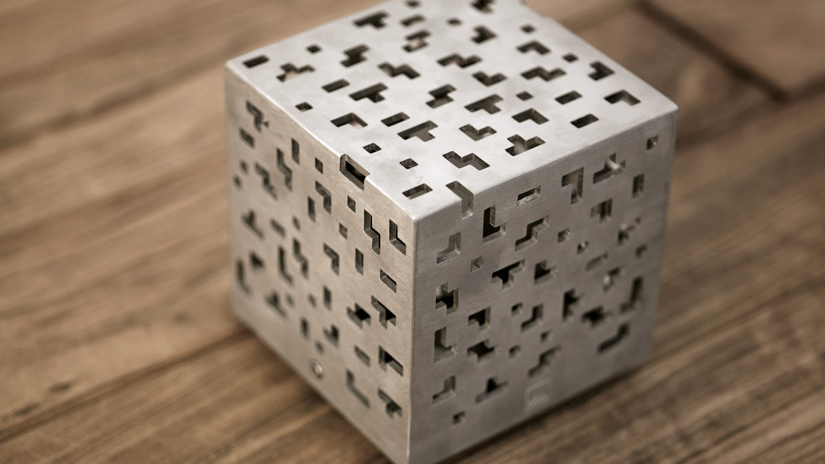 Stainless steel AMS cube lamp with a cut-out pattern on a wooden surface