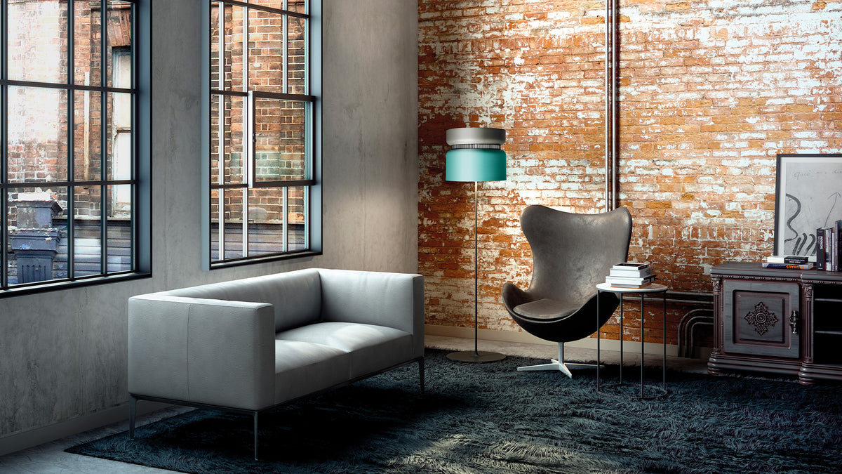 B.lux Aspen floor lamp with a teal shade beside a grey sofa and an egg chair in a brick loft