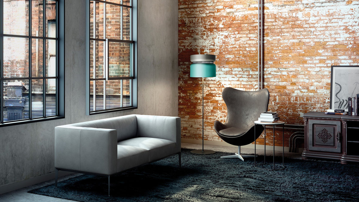 B.lux Aspen floor lamp with a teal shade beside a grey sofa and an egg chair in a brick loft
