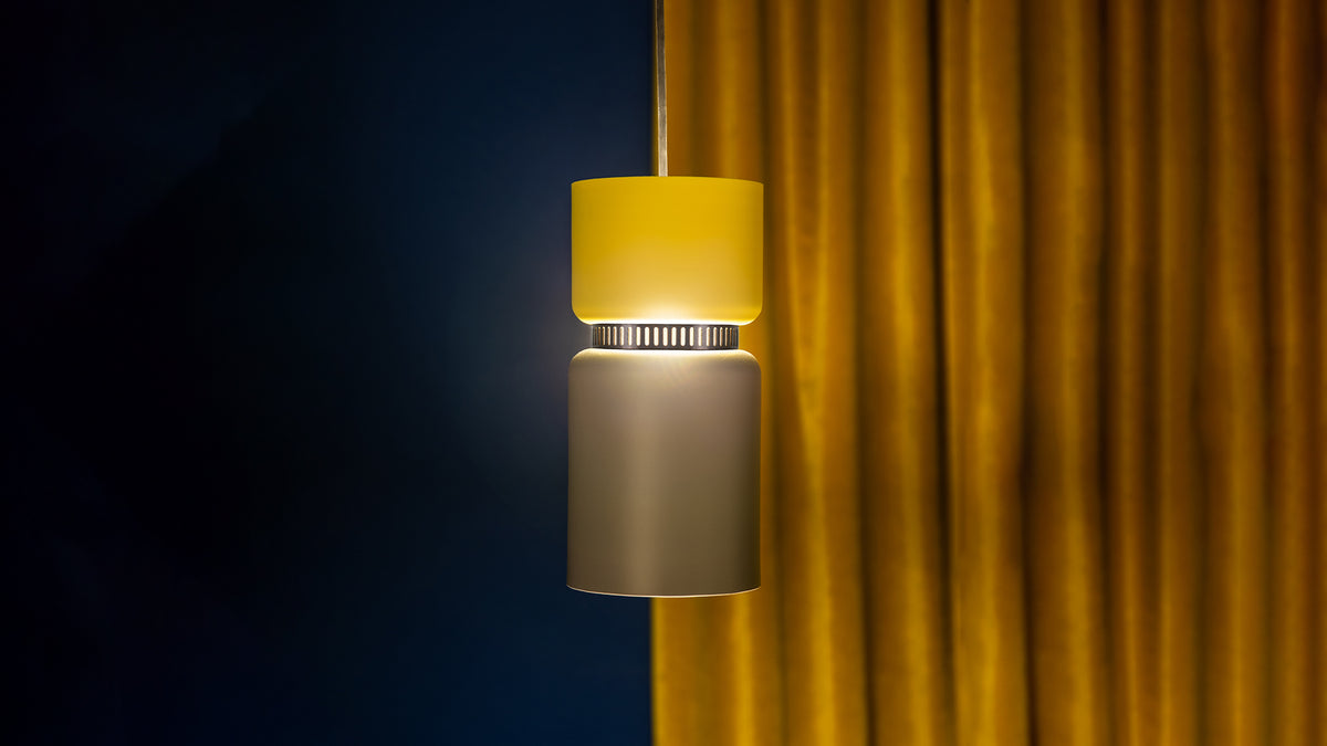 B.lux Aspen pendant with a yellow top shade and brass bottom shade against dark curtains