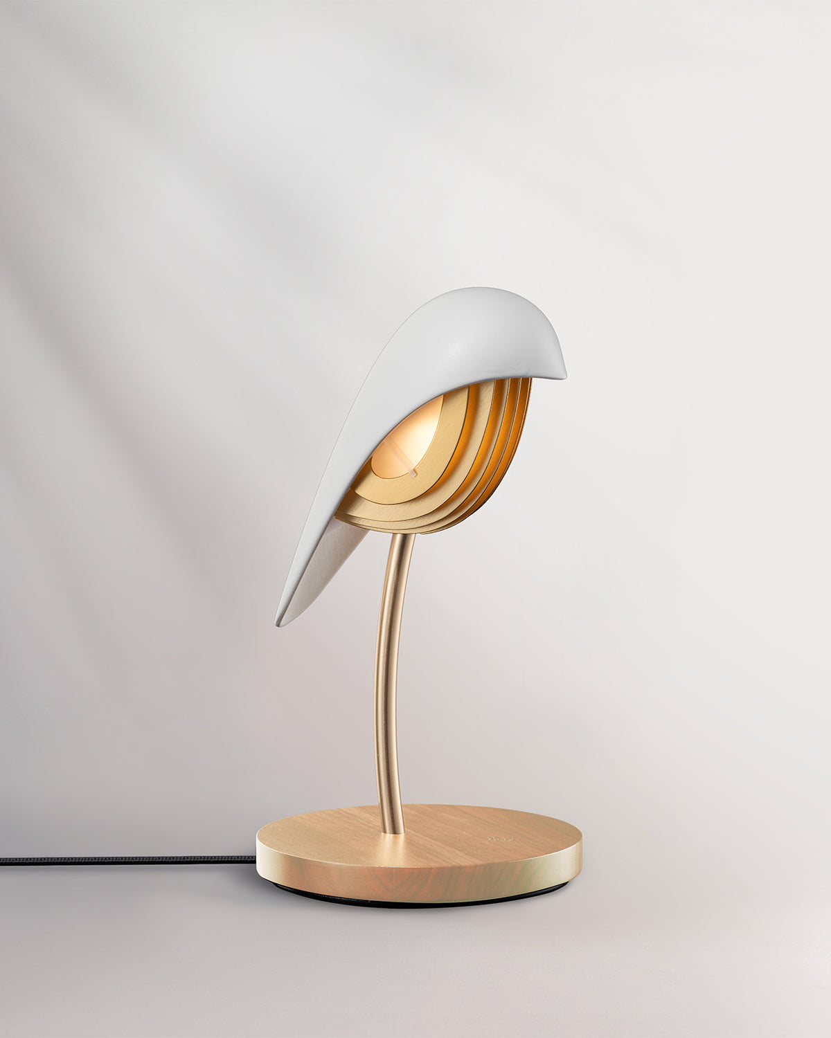 Daqiconcept Bird Ivory White lamp glowing warm on a pale desk