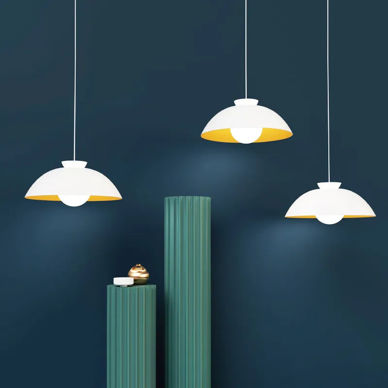 Three pendant lights hanging against a dark blue wall with green cylindrical objects.