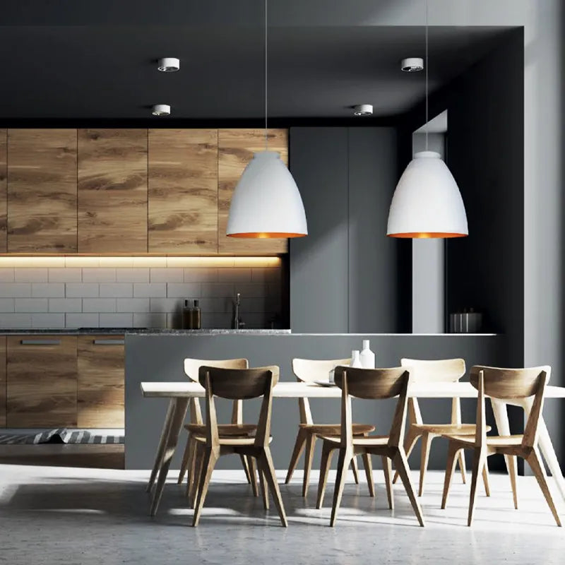 Modern kitchen with wooden cabinets, white pendant lights, and a dining table.