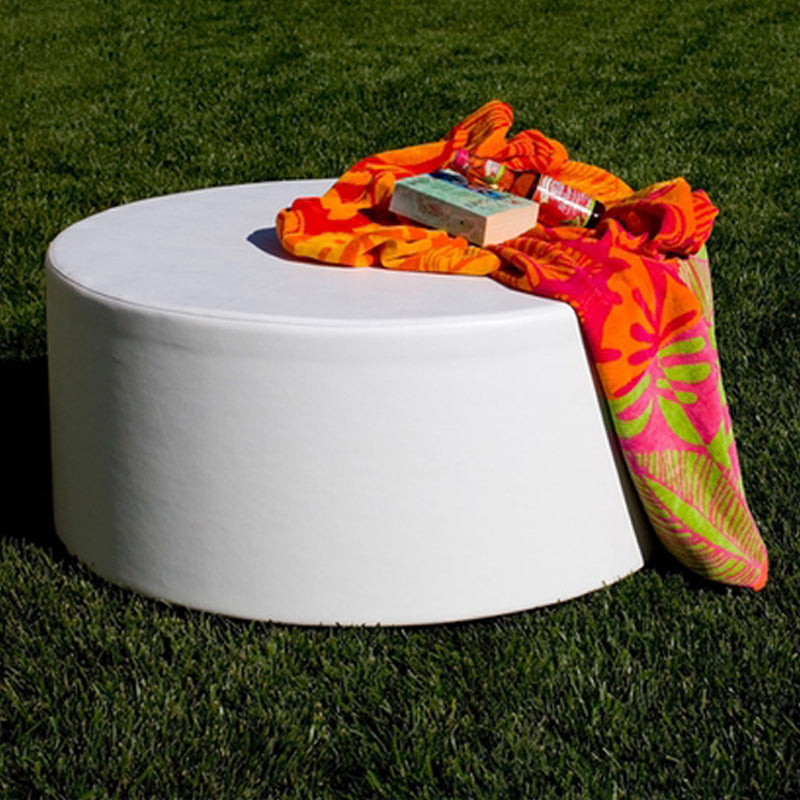 White Puck round ottoman on a lawn with an orange and pink towel and a drink on top