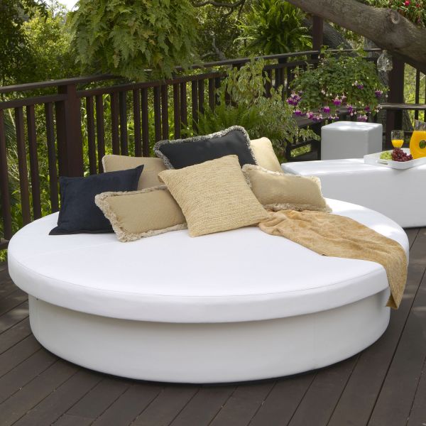 White round Sun Pad daybed on a wooden deck with dark pillows and a woven throw