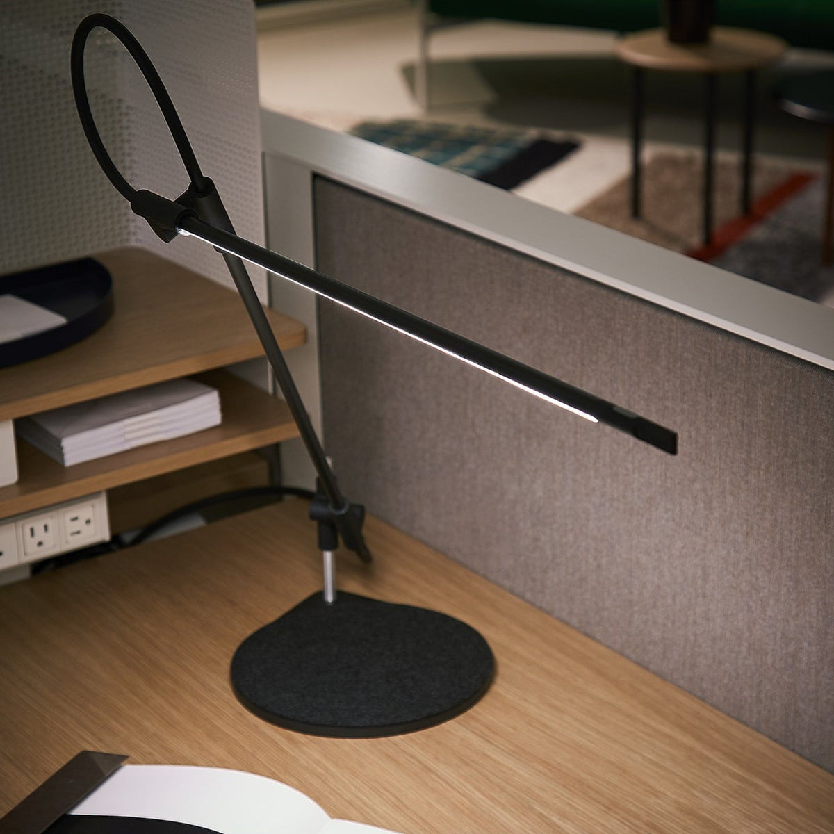 Superlight desk task lamp lighting a work surface in a furnished room