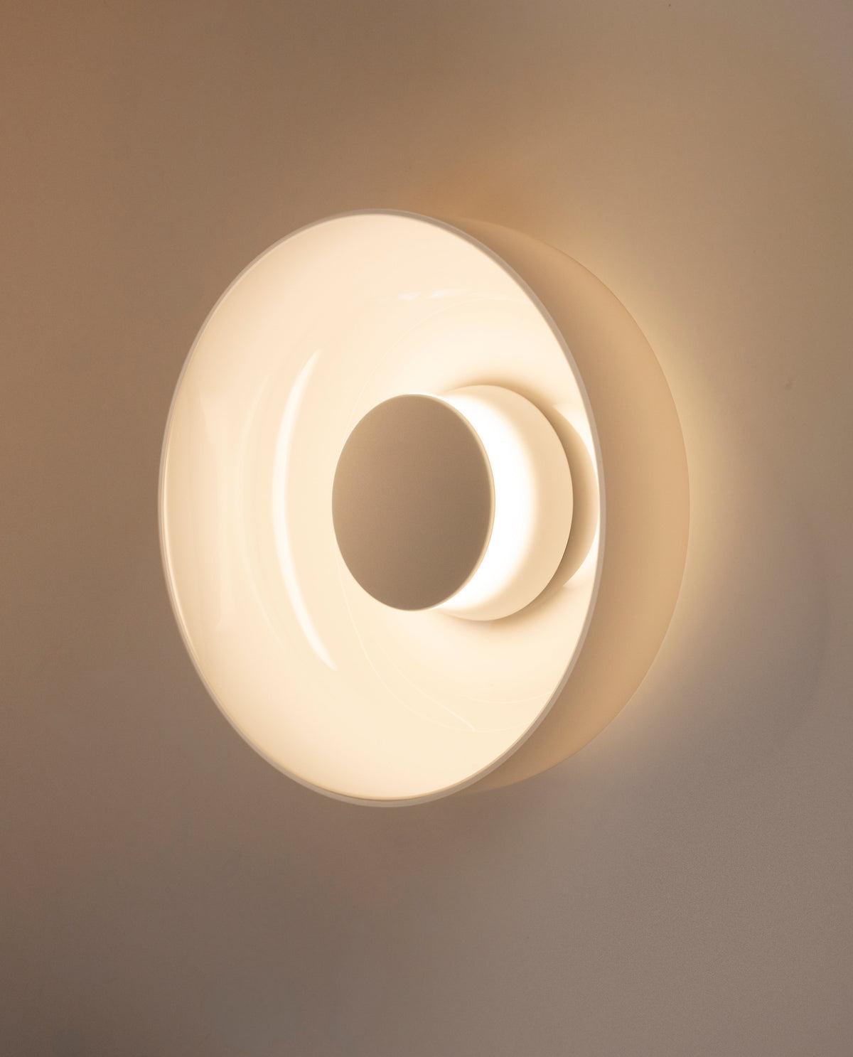 Round opal glass wall sconce glowing warm against a tan wall, in-situ photo