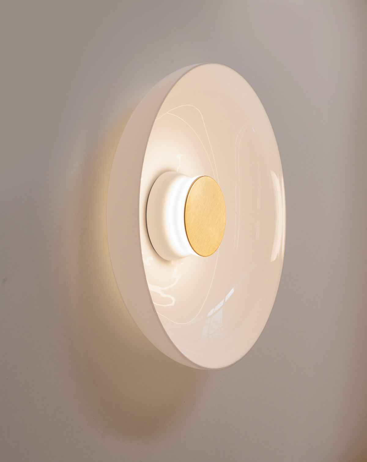 Opal glass sconce with brass faceplate glowing on a grey wall, close view