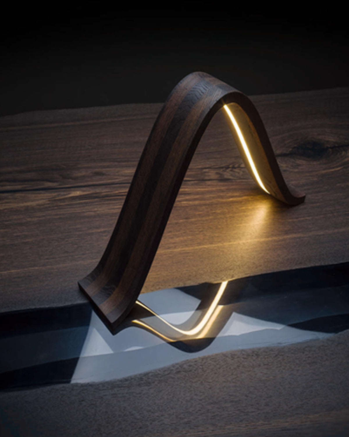 Teukho Lambda fossil oak LED table lamp in Black lit on a wood desk