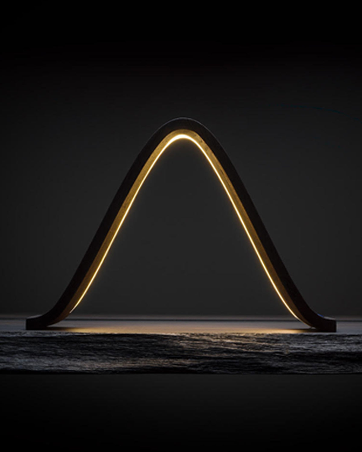 Teukho Lambda fossil oak LED table lamp in Black glowing on a dark stone surface