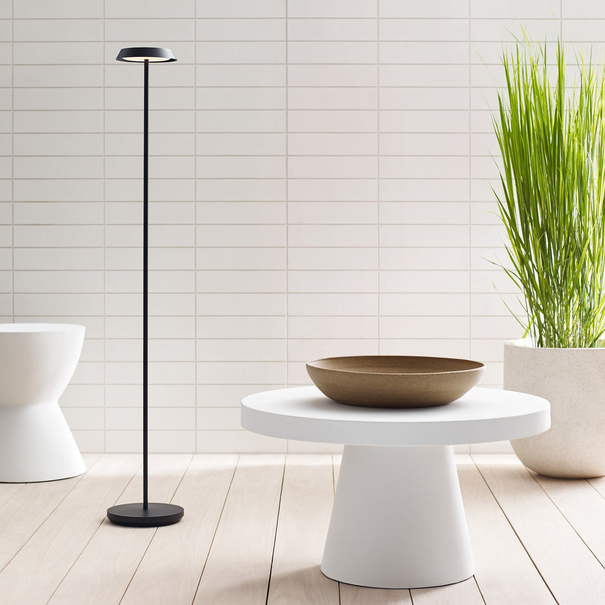 Tepa Medium cordless floor lamp in Black glowing beside a chair