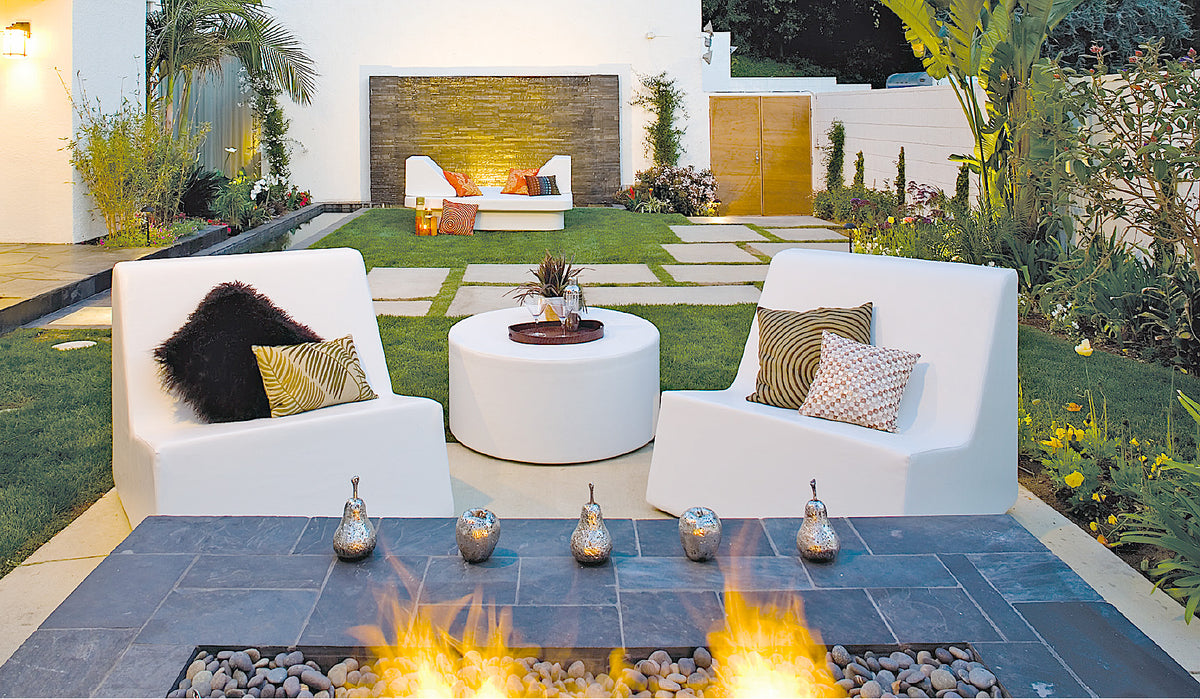 Two white Check lounge chairs flanking a round white ottoman beside a fire pit in a courtyard garden
