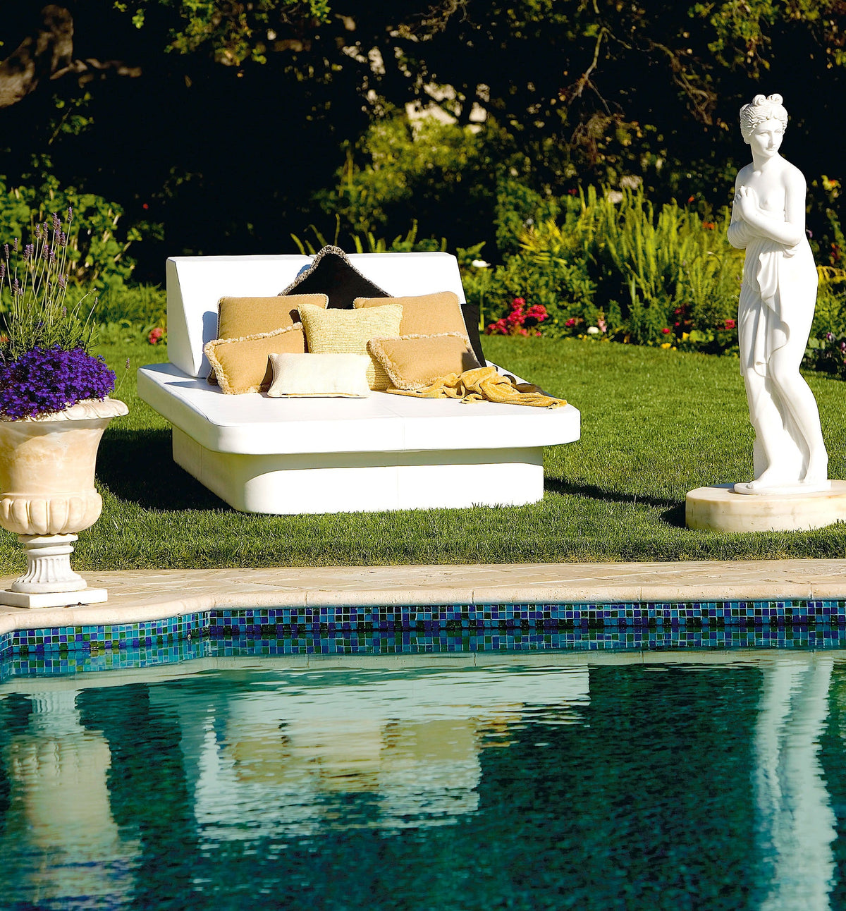 White Crib queen daybed with Lean wedge headboards and tan pillows on a lawn beside a pool with a classical statue