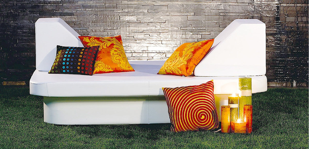 Crib daybed with two Lean wedge headboards, orange and patterned pillows and candles against a dark stone wall
