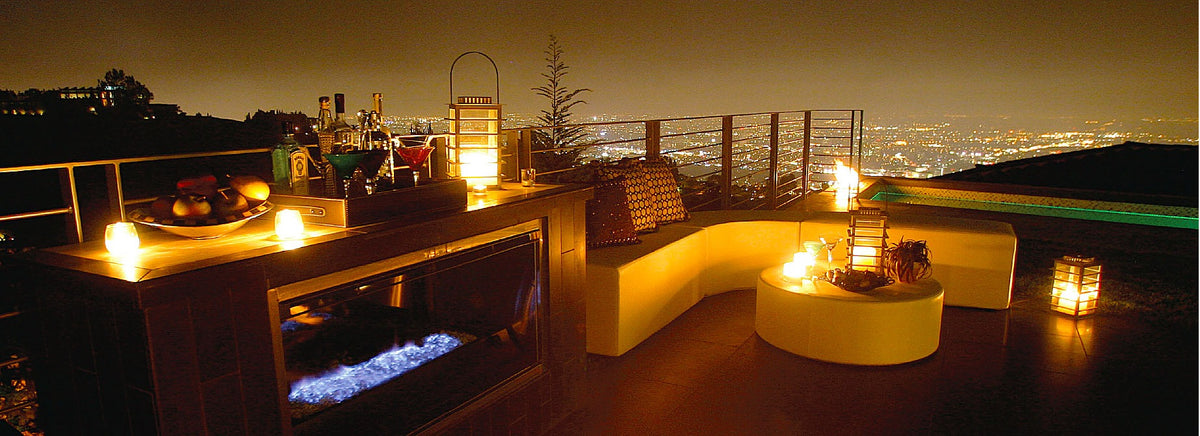 White Puck round ottoman beside a bench and fire table on a night-time terrace overlooking city lights