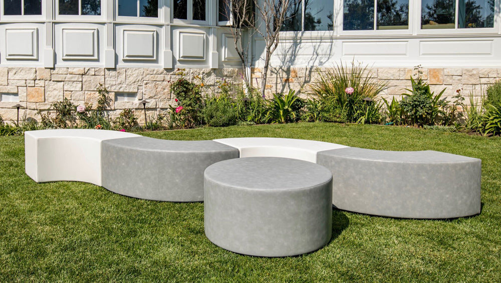 The Ring curved benches and round ottoman in white and gray vinyl arranged on a garden lawn beside a planted border