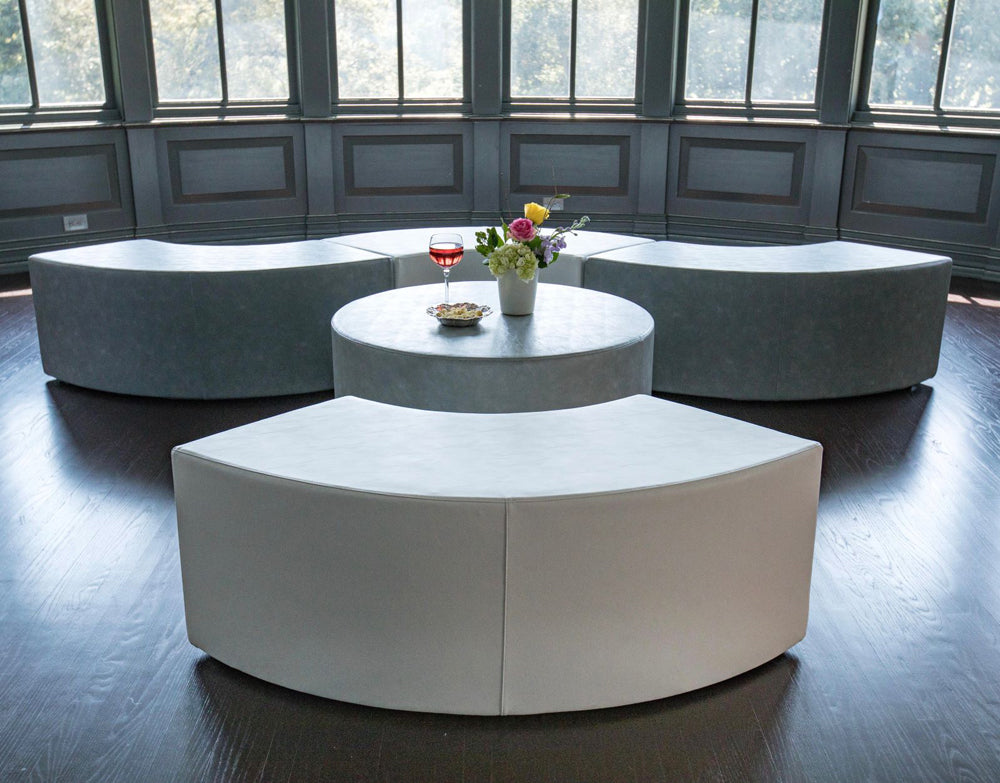 The Ring curved gray and white vinyl benches circling a round ottoman in a lounge with tall windows