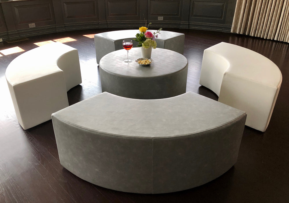 The Ring with two white and two gray curved vinyl benches around a round gray ottoman on a dark wood floor