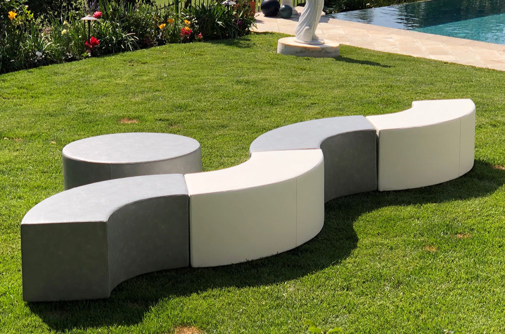 The Ring curved benches linked in an S-curve on a lawn beside a pool, with the round ottoman set apart