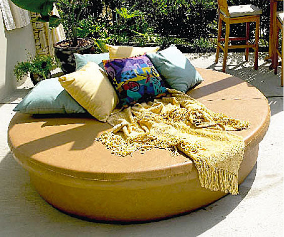 Round Sun Pad in tan vinyl dressed with throw pillows and a woven throw on a patio