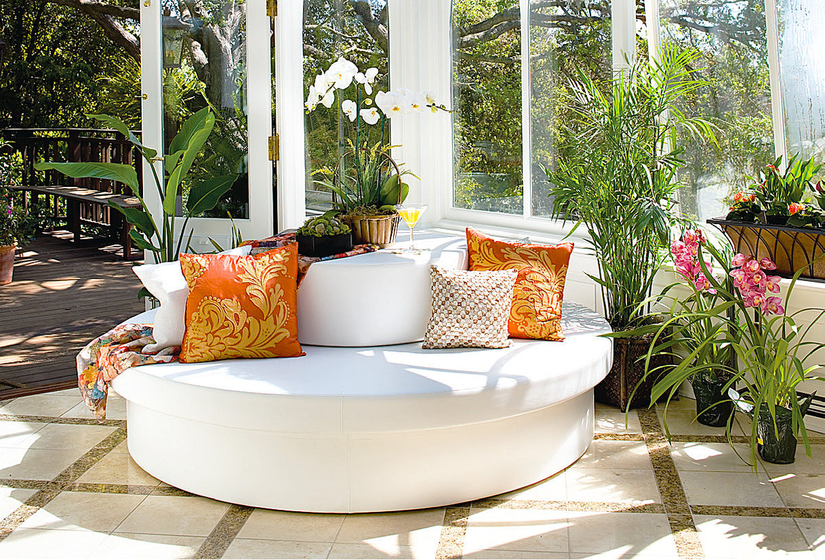 Round white vinyl Sun Pad with a Stack drum, orange and cream pillows in a sunroom opening to a patio