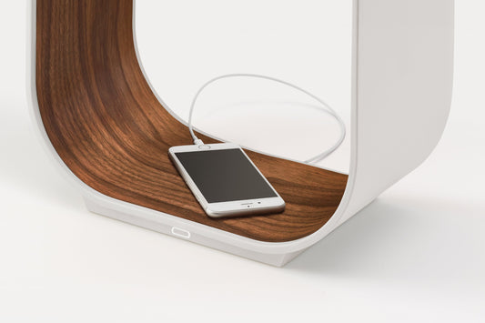 Pablo Designs Contour Large table lamp with a phone resting in its wood-lined tray